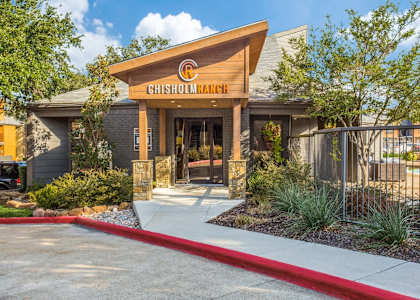 The Chisholm Ranch building has a wooden entrance with a red walkway leading to it.