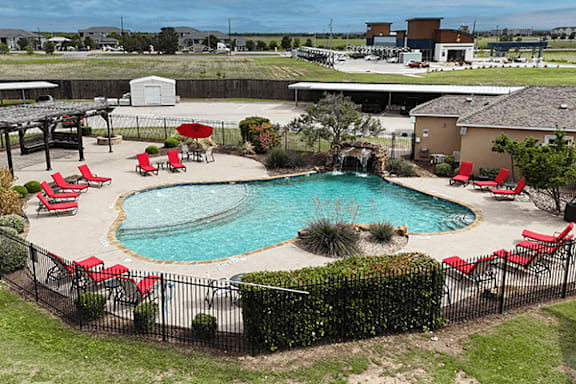 A pool surrounded by red chairs and a black fence.