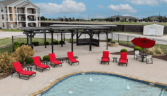 A pool with red chairs and a black fence.