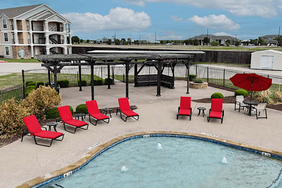 A pool with red chairs and a table with a red umbrella.
