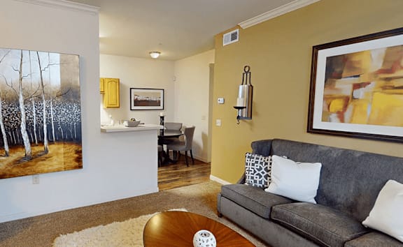 A living room with a grey couch and a painting on the wall.
