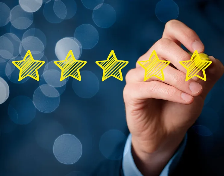 A hand holding a glowing five-star rating, symbolizing excellence and quality, set against a soft blue bokeh background.
