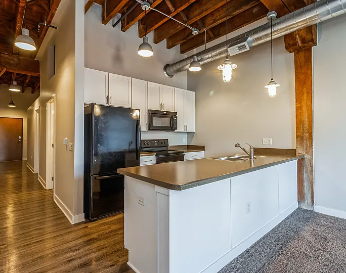 Modern loft kitchen with industrial lighting, sleek black appliances, and polished wooden ceiling beams.