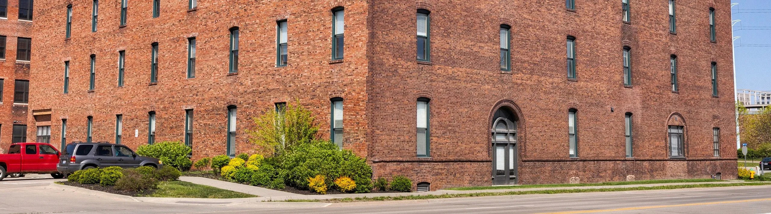 Charming historic brick building with large windows, ideal for lofts or offices, featuring lush landscaping and ample parking.