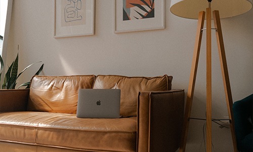 Leather couch with a laptop and floor lamp next to it.