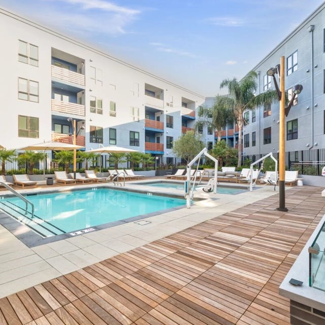 Outdoor swimming pool with lounge chairs and umbrellas surrounded by apartment buildings.