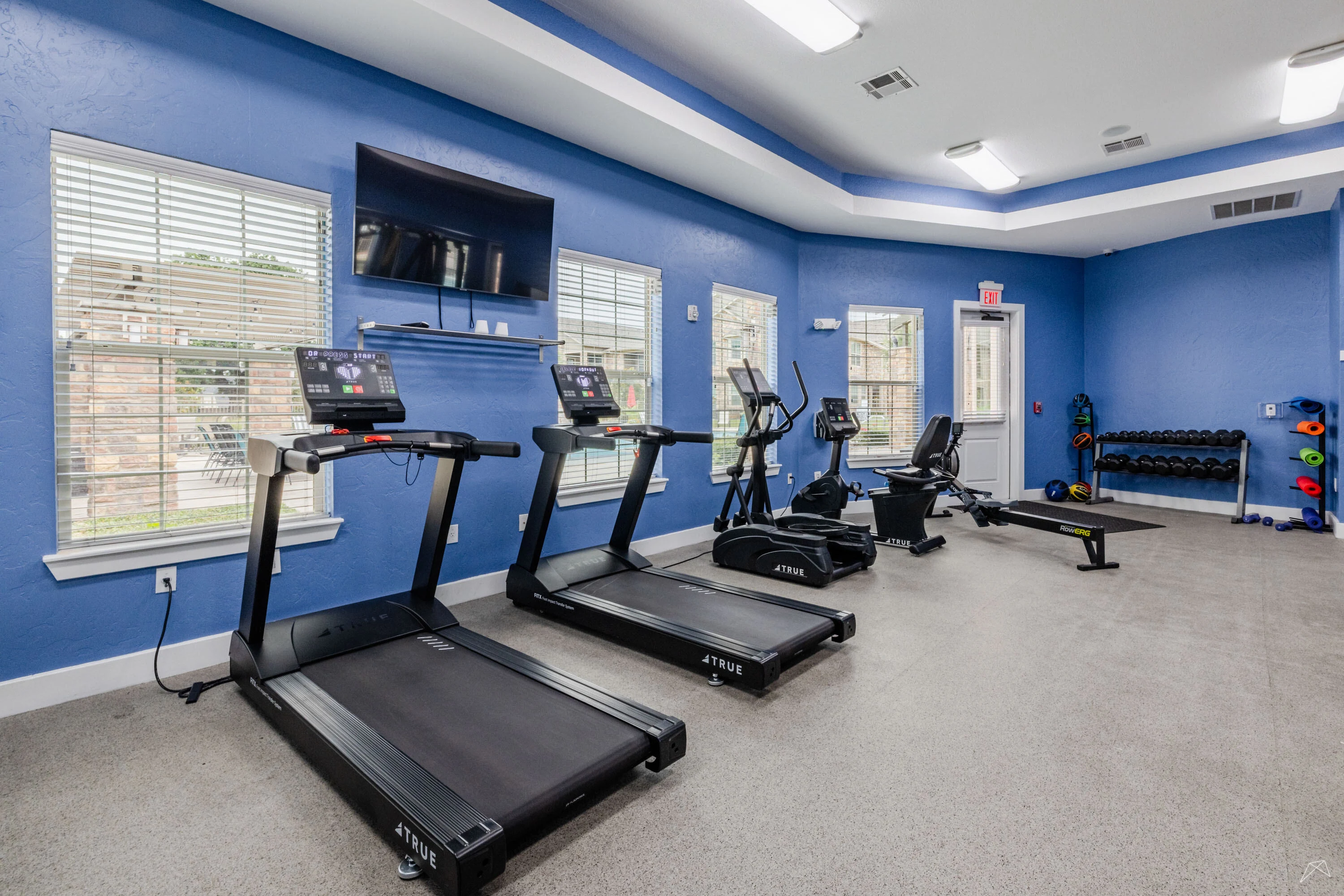 Bright fitness center featuring treadmills, strength training equipment, and large windows.
