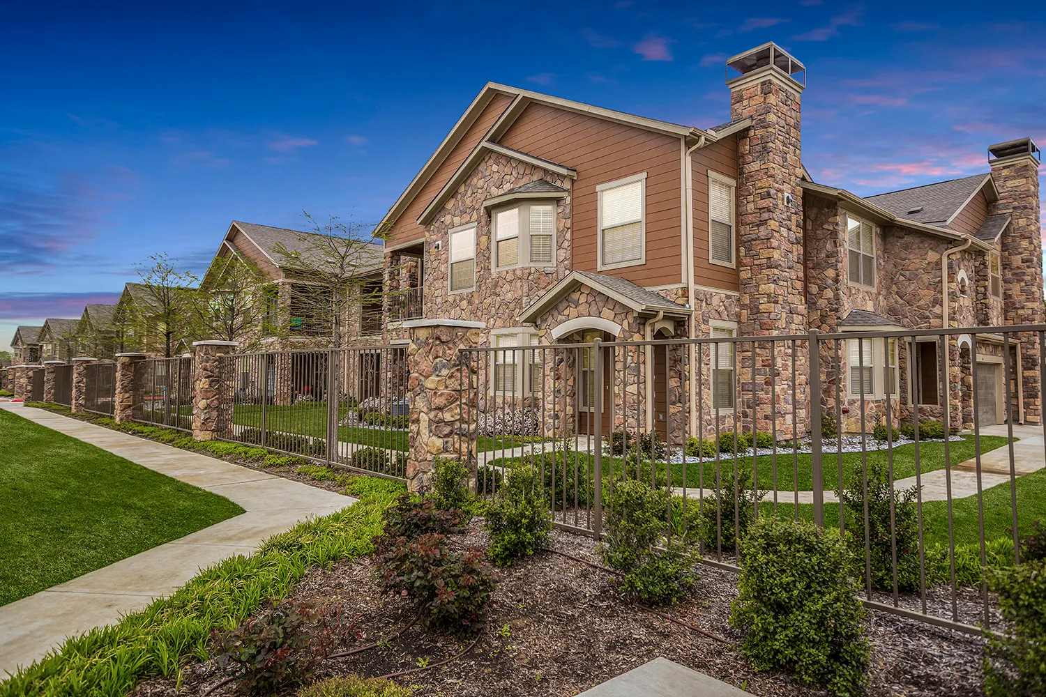 Building exterior with burnt orange siding, brown stone, and a brown metal fence surrounding