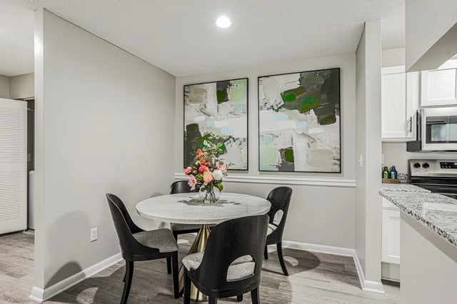 Dining area with a marble-top table and four chairs, featuring modern art on the wall and a glimpse of the kitchen.
