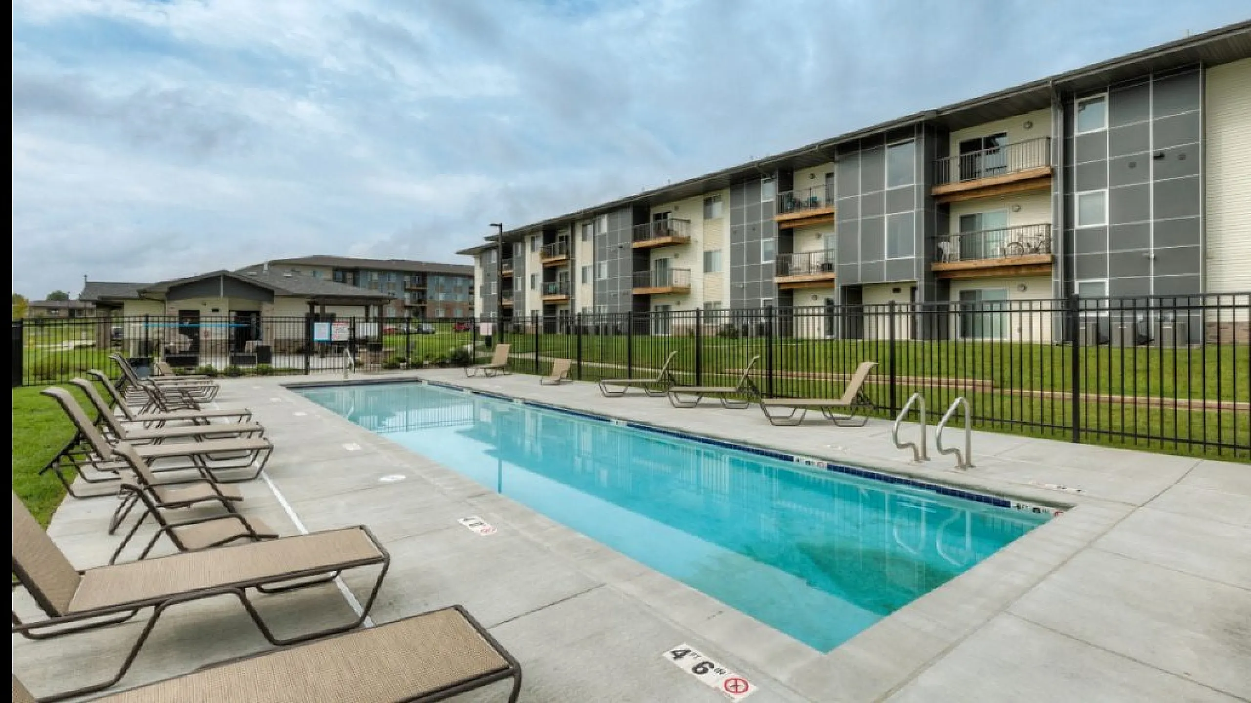 Modern apartment complex with inviting swimming pool, sun loungers, and lush green surroundings for a relaxing lifestyle.
