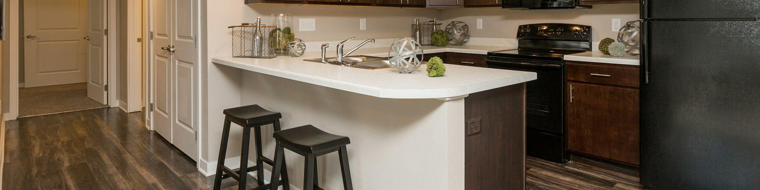 Modern kitchen with sleek dark cabinets, a spacious island with bar stools, and elegant lighting in a stylish apartment setting.