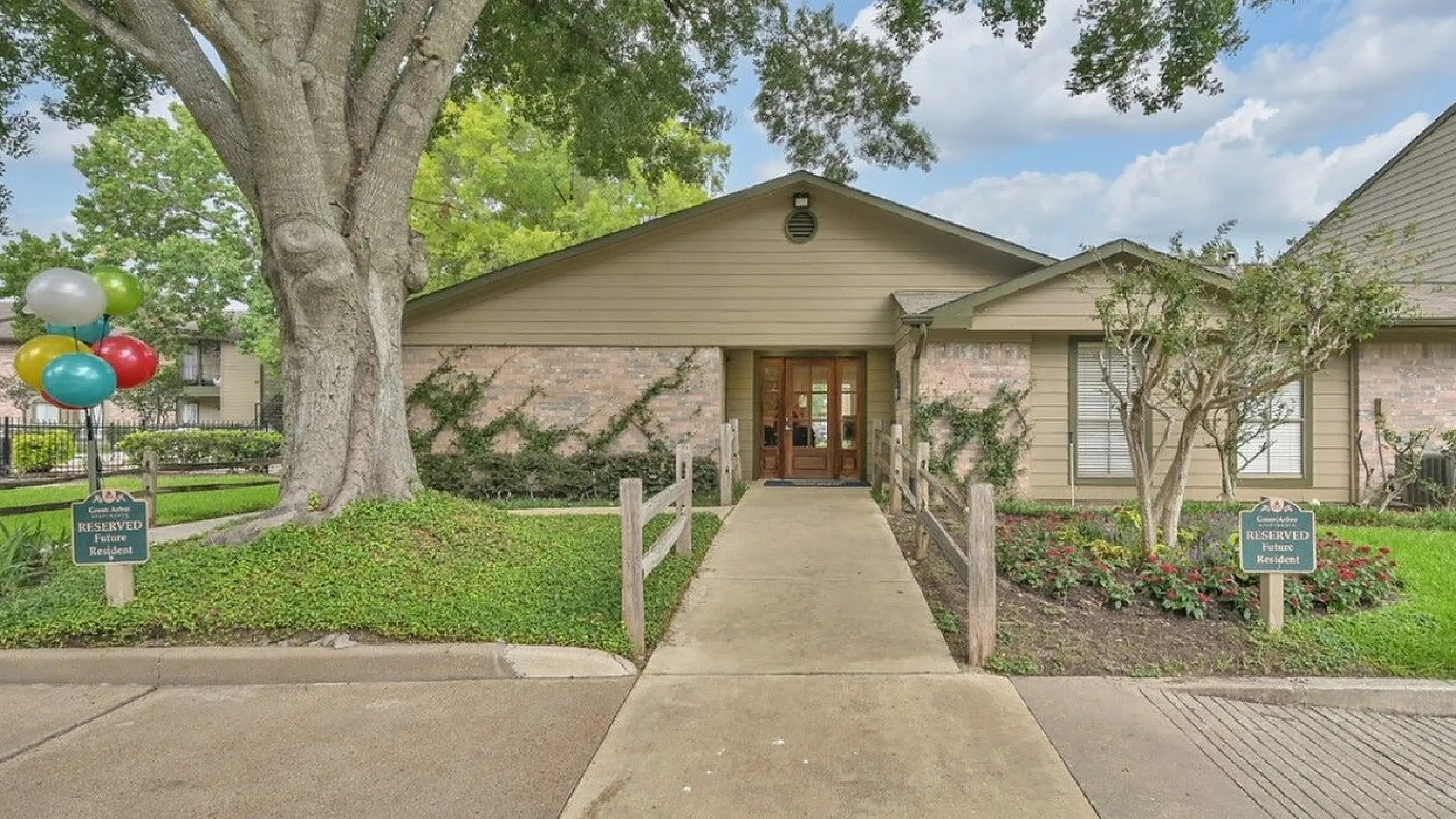 Charming apartment entrance with lush greenery, vibrant balloons, and welcoming reserved parking, offering a serene living environment.