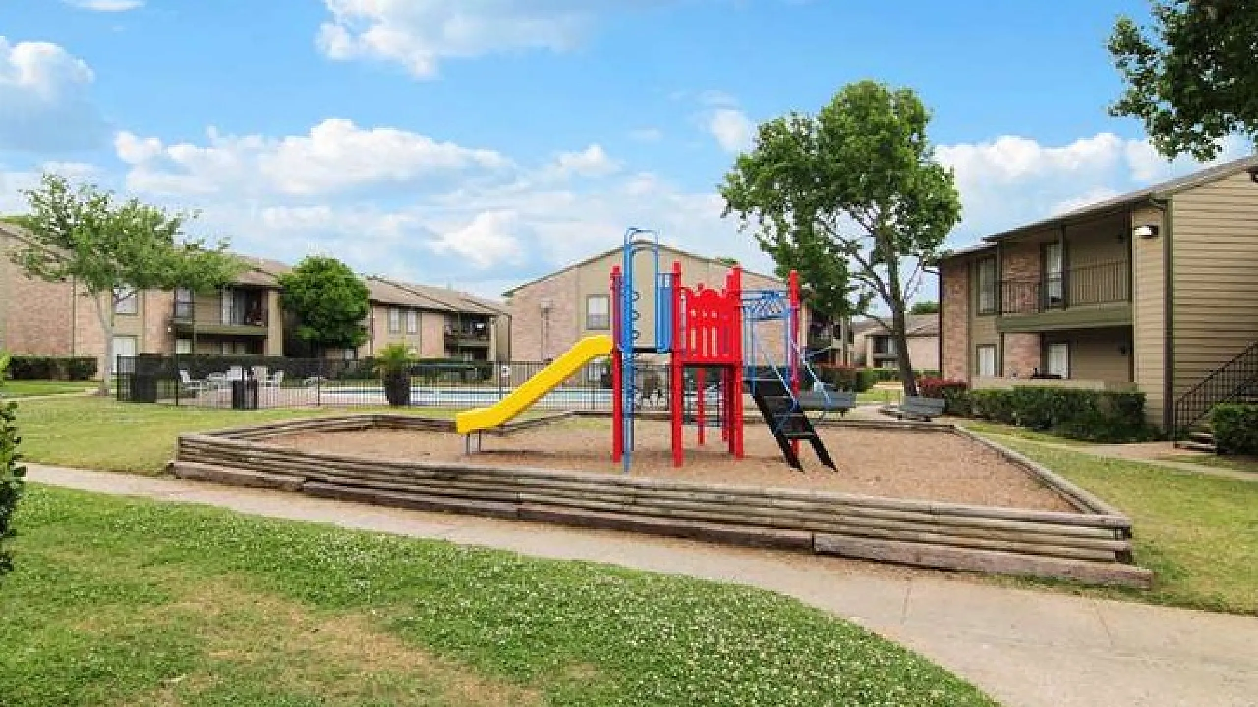 Inviting apartment complex featuring a vibrant playground surrounded by lush greenery, perfect for families and outdoor enjoyment.