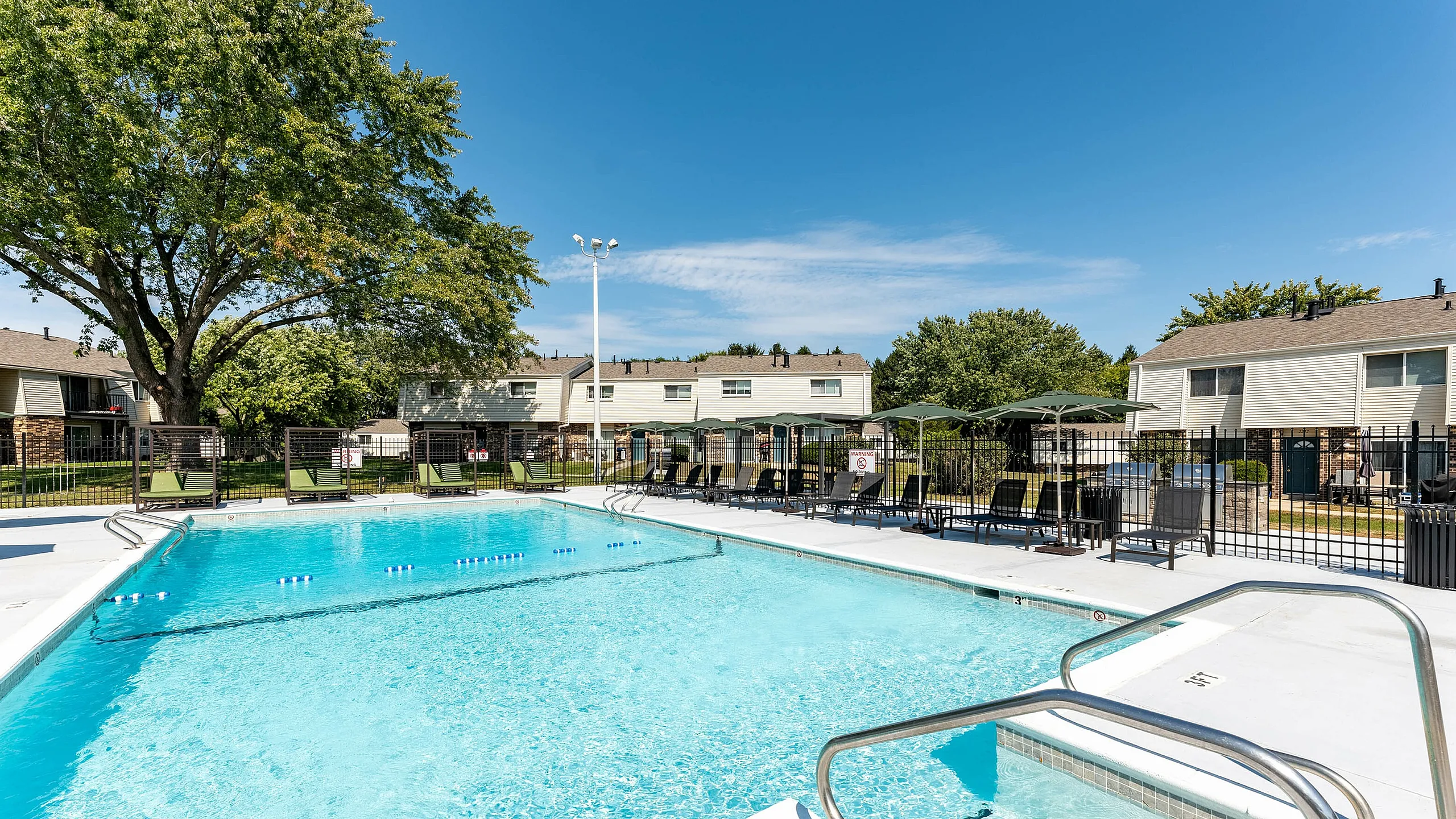 Inviting outdoor swimming pool area with sun loungers, umbrellas, and lush greenery, perfect for relaxation in a friendly community setting.