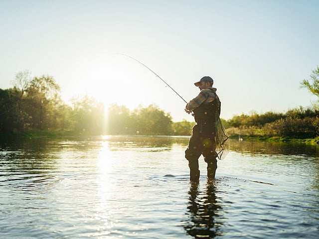 Serene scene of an angler fishing in a tranquil river under a bright morning sun.