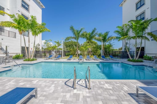 Apartment complex swimming pool with lounge chairs and palm trees.