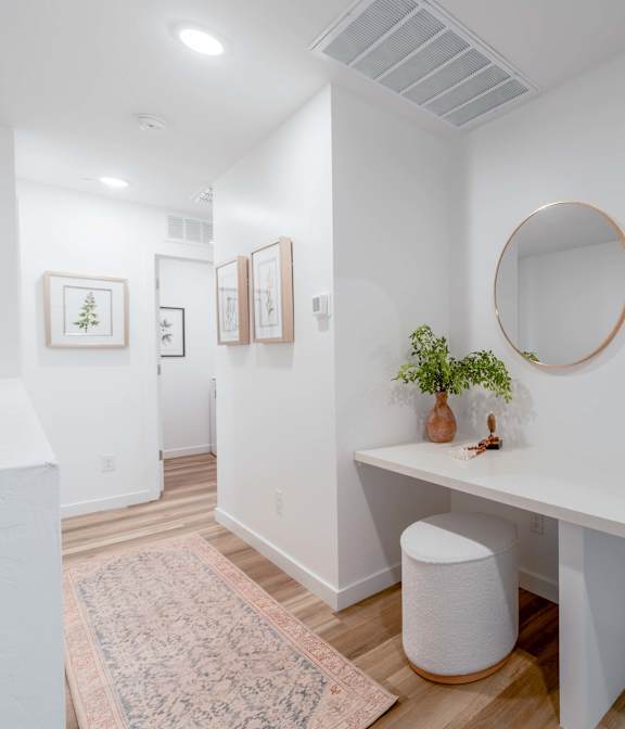 A white room with a round mirror and a desk with a plant on it.