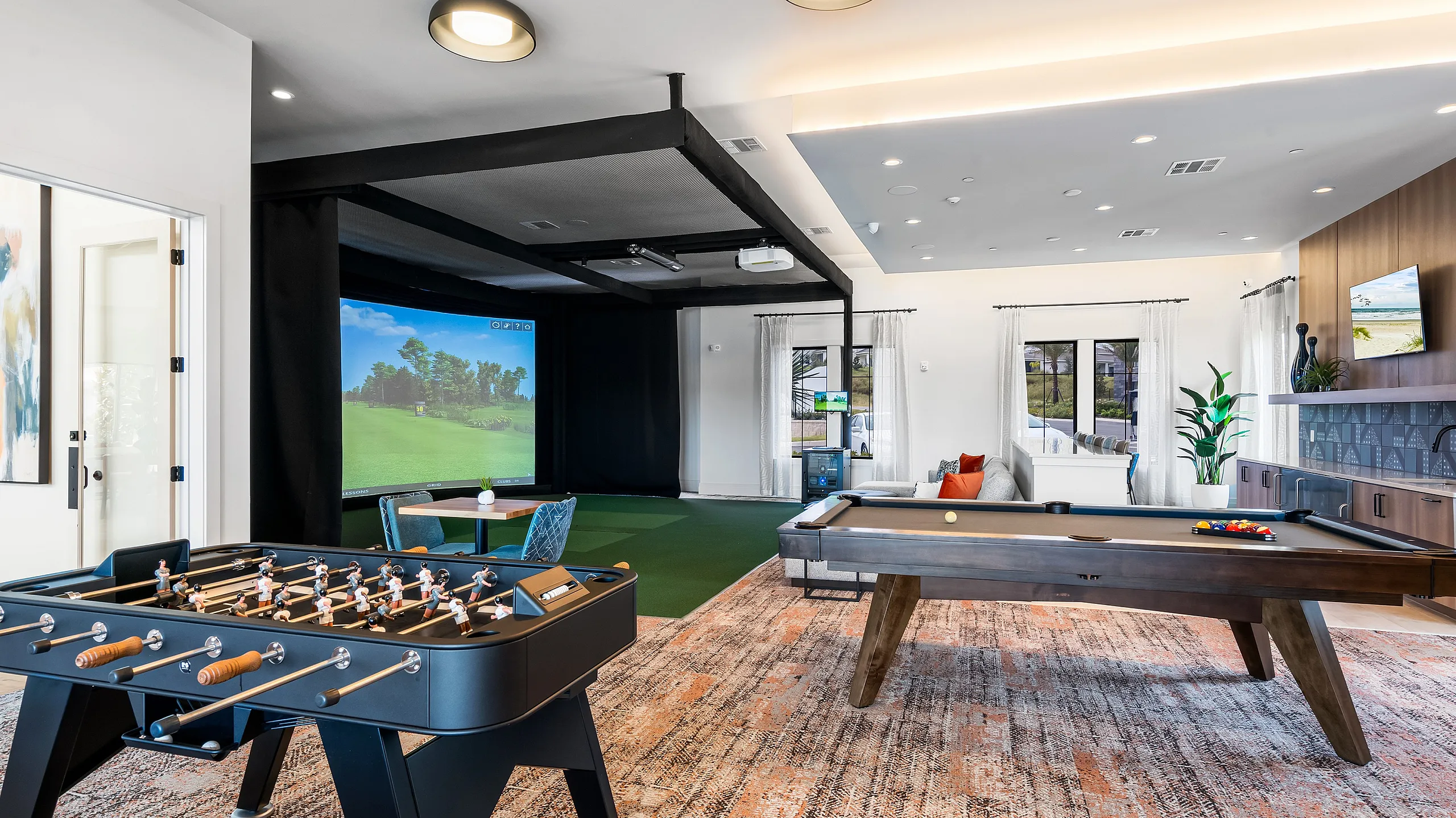 Luxurious entertainment room with a pool table, foosball table, and a golf simulator, accented by modern decor and plush seating.
