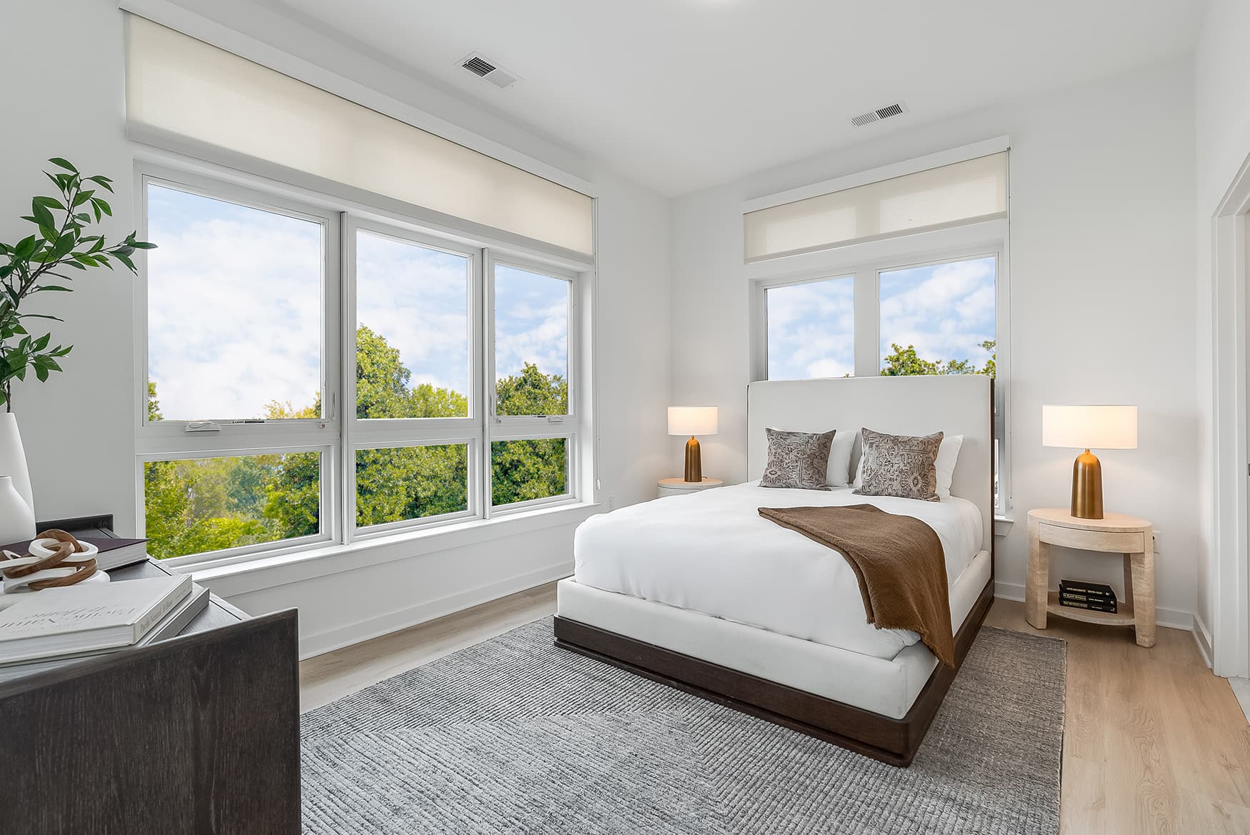 Bright primary bedroom at Livana Fair Lawn with large windows, modern furnishings, and serene treetop views.