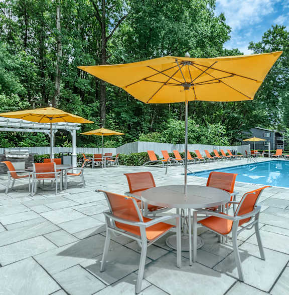 A poolside table with chairs and umbrellas is set up next to a pool at Crest at East Cobb Apartments, Georgia