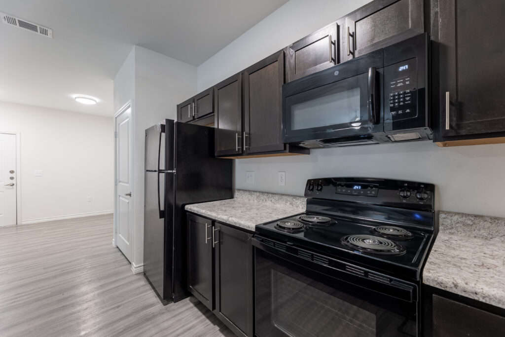 Spacious kitchen equipped with black appliances, granite countertops, and modern brown cabinets.