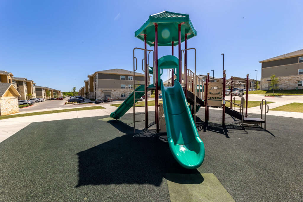 A playground including two green slides and climbers at Sansom Bluff Apartments in Fort Worth.