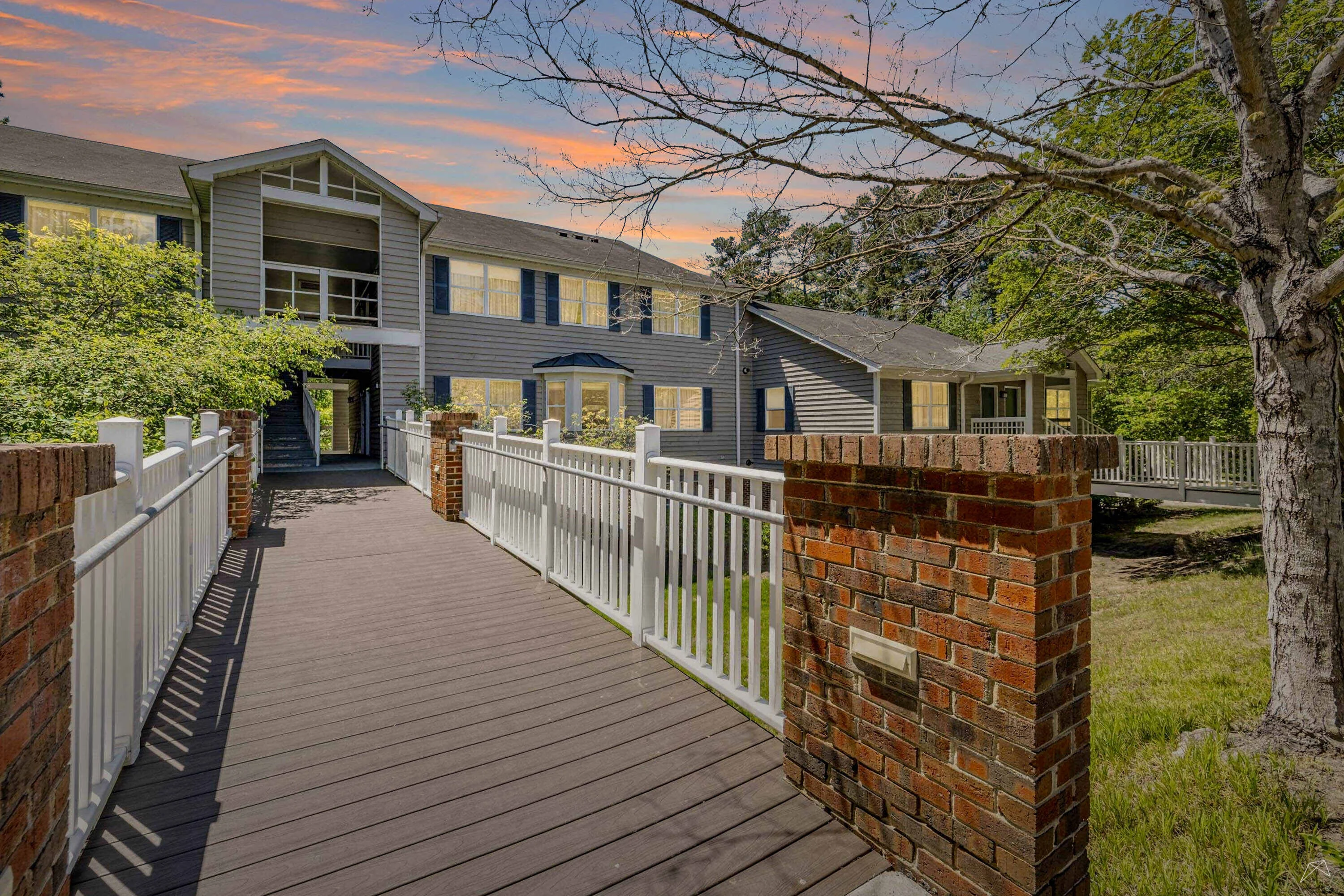 Apartment entrance with a wood-style walkway, light color fencing, and sunset hues in the sky.