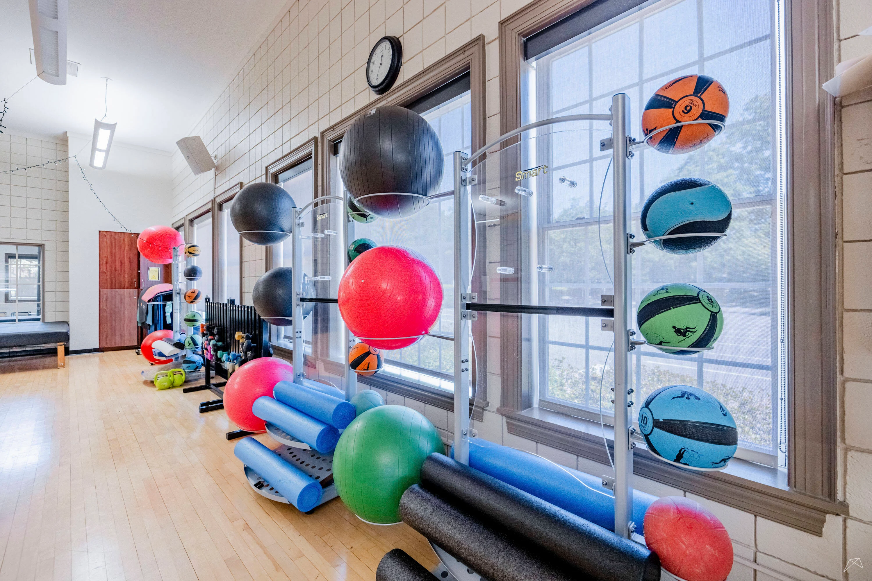 Bright fitness room featuring exercise balls, mats, and equipment near large windows.