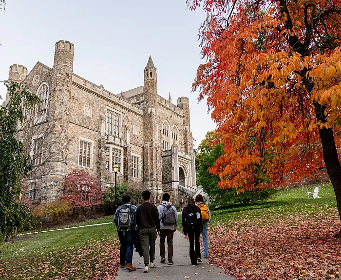 Charming stone building surrounded by vibrant autumn foliage, with people strolling on the walkway.