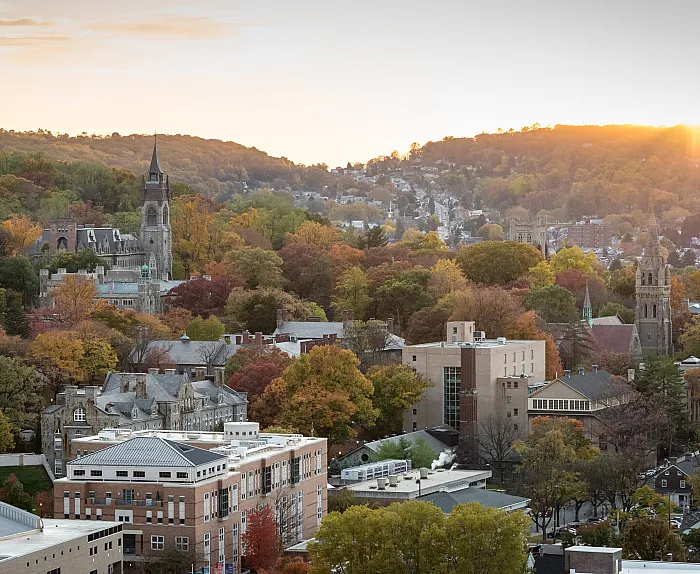 Breathtaking view of a charming townscape bathed in golden sunset light, surrounded by lush autumn foliage and historic buildings.