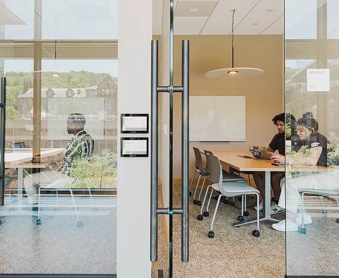 Modern glass-walled breakout room featuring natural light, vibrant outdoor views, and a collaborative workspace with sleek furniture.