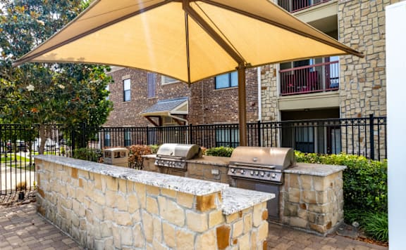 A patio with a stone wall and a grill under a yellow umbrella.