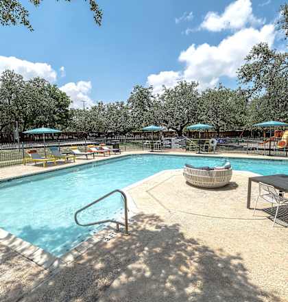 A large outdoor swimming pool surrounded by trees and a fence.