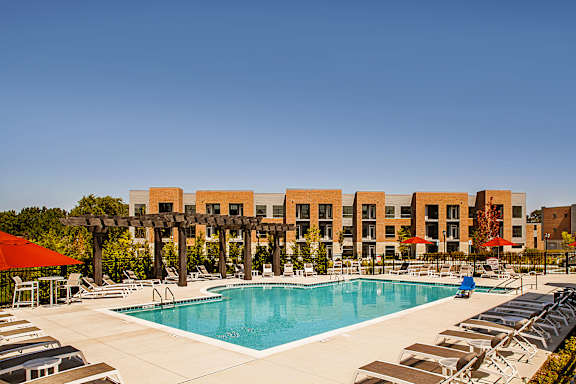 A large swimming pool surrounded by sun loungers and umbrellas in front of a building.