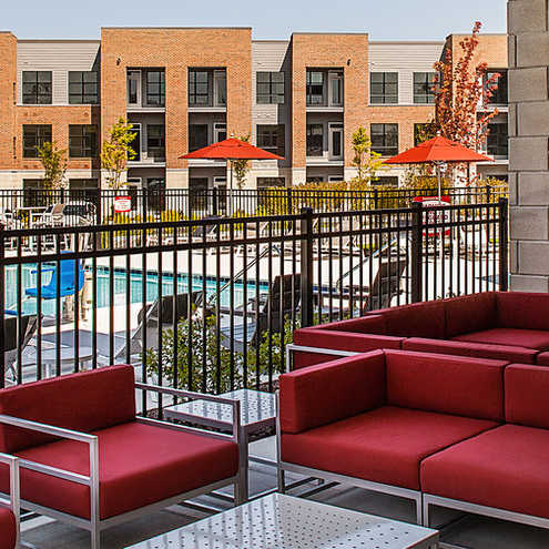 A patio with red chairs and a pool in the background.
