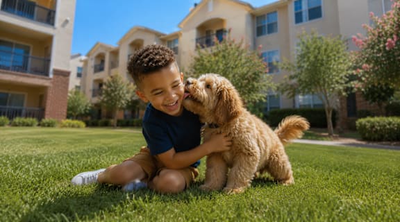 A boy is hugging a small dog on a grassy lawn.