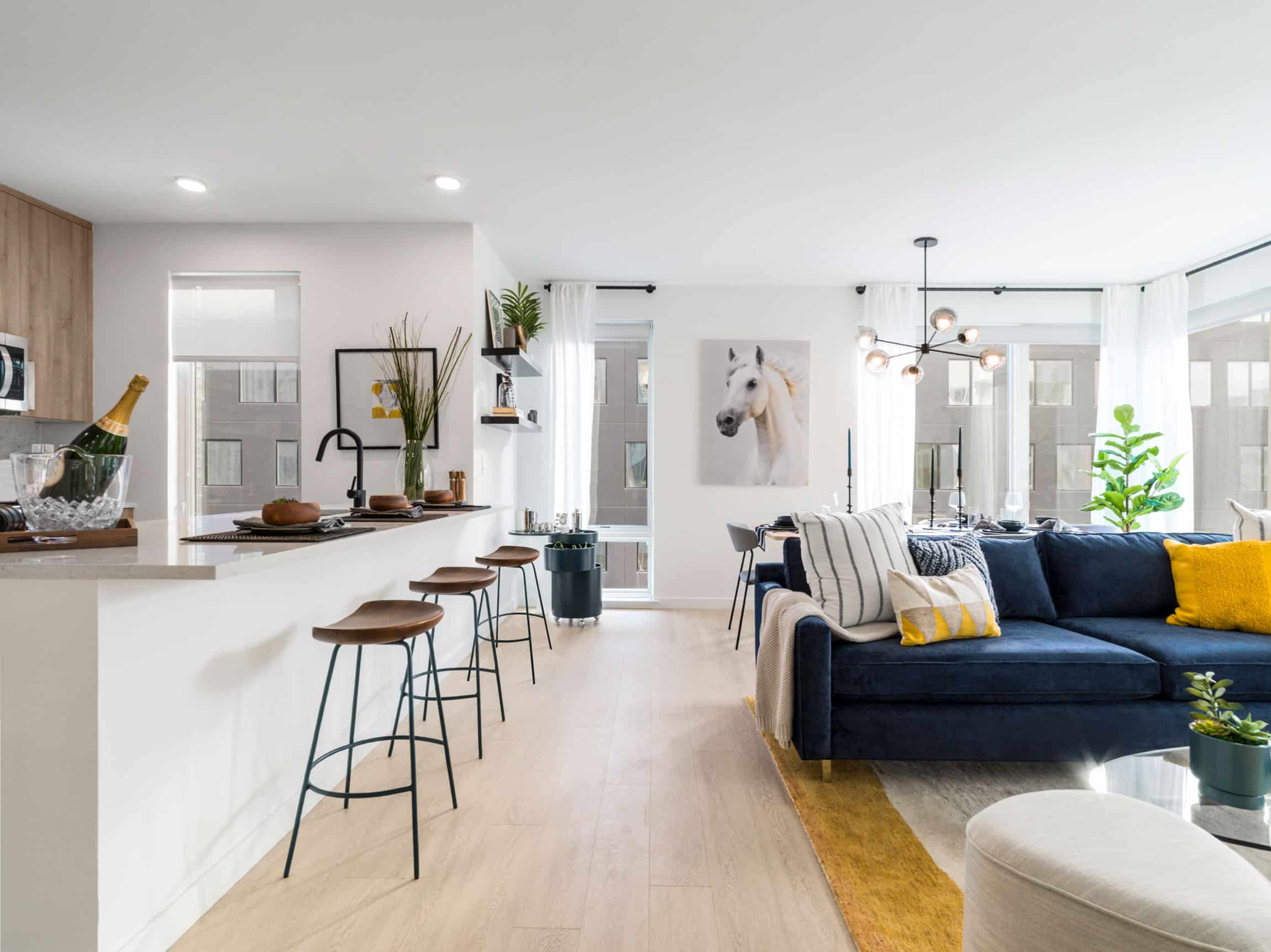 luxury apartment interior with white kitchen island with seating, blue couch, modern chandelier, picture of a white horse and large windows