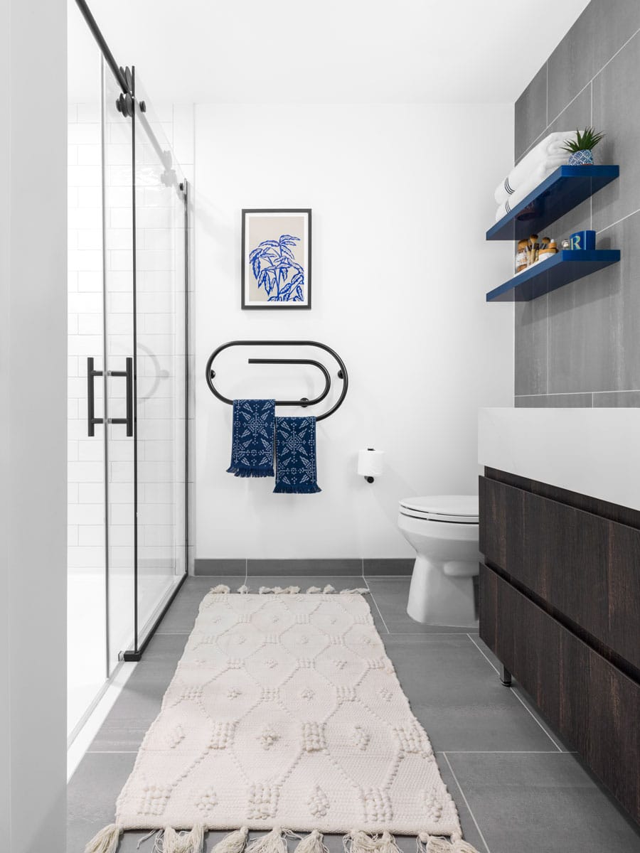 luxury apartment bathroom with glass shower door, dark cabinet and gray tile wall