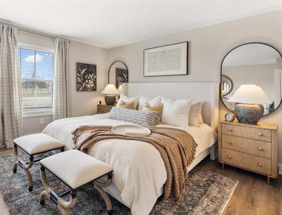 Spacious primary bedroom in single-family rental home at Mural Lewis Center featuring large windows, plush bedding, neutral tones, wall art, and soft carpeting