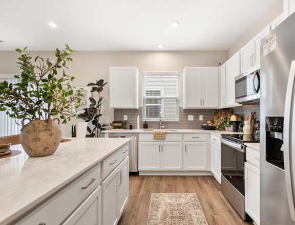 Bright modern apartment kitchen at Mural Lewis Center featuring white shaker cabinets, quartz countertops, stainless steel appliances, kitchen island, and wood-style flooring