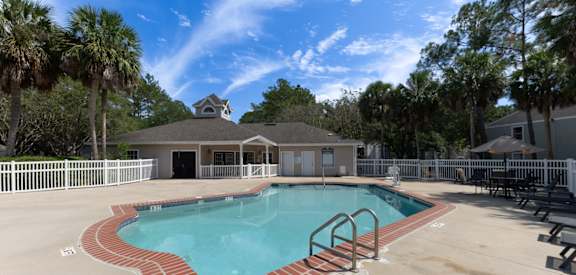 A pool with a brick border and a house in the background.