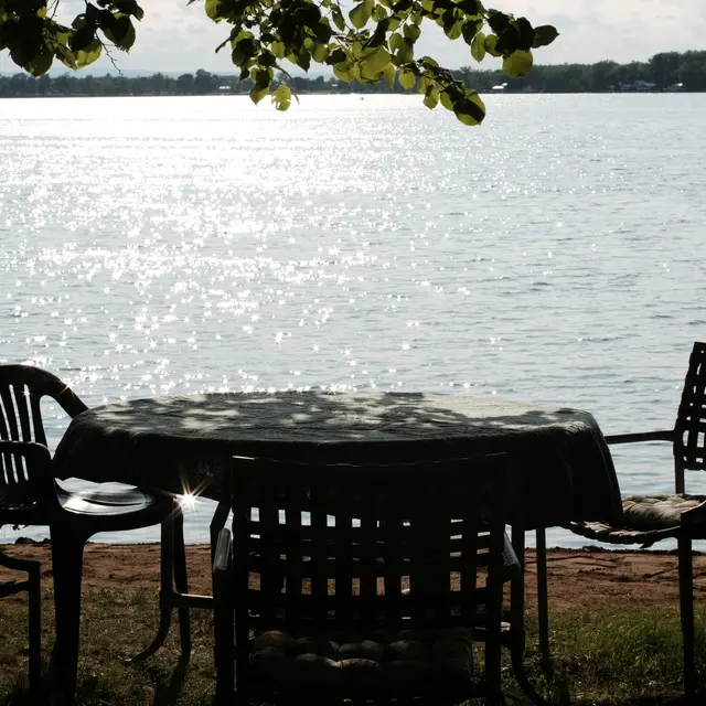 A table and chairs set beside a calm lake with sparkling water in the background.