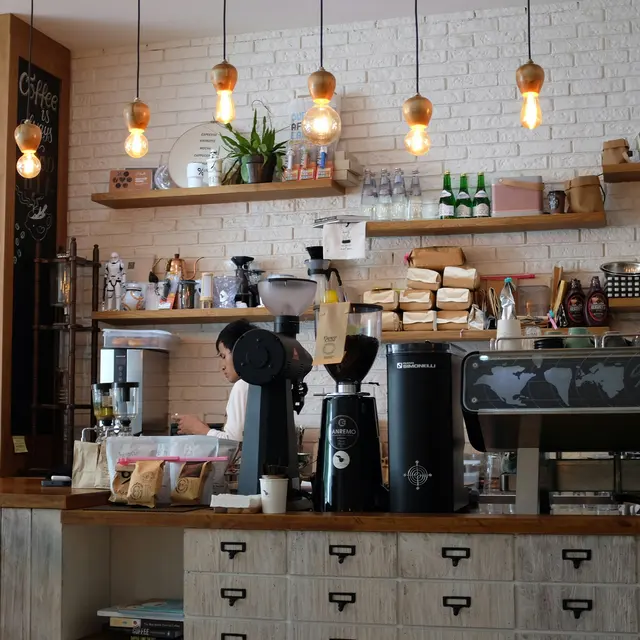 A cozy coffee shop interior with a wooden counter, an espresso machine, and warm lighting from hanging bulbs.