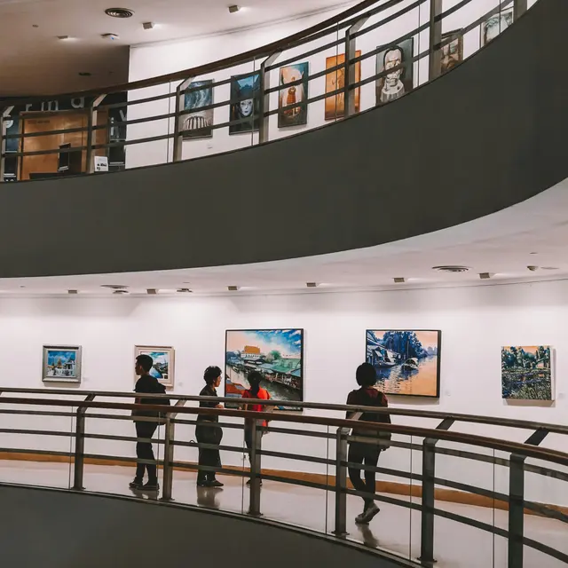 Visitors walking through an art gallery with paintings displayed on the walls.