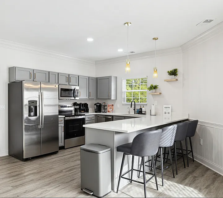 Modern kitchen with sleek stainless steel appliances, spacious gray cabinetry, and a stylish island with seating for four under elegant pendant lighting.