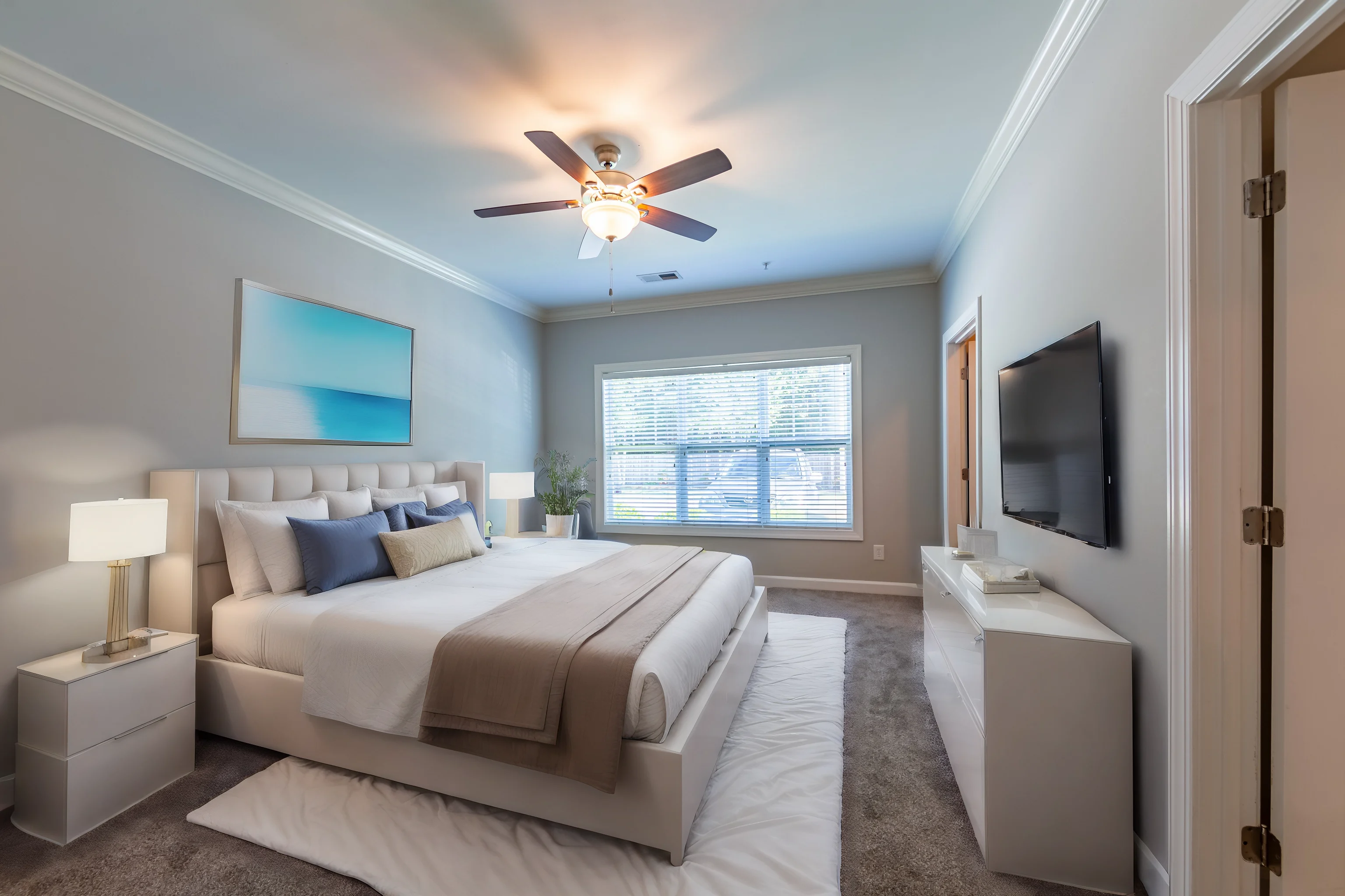 A modern bedroom featuring a large bed with neutral bedding, two nightstands with lamps, a wall-mounted TV, and a sunny window with a view.