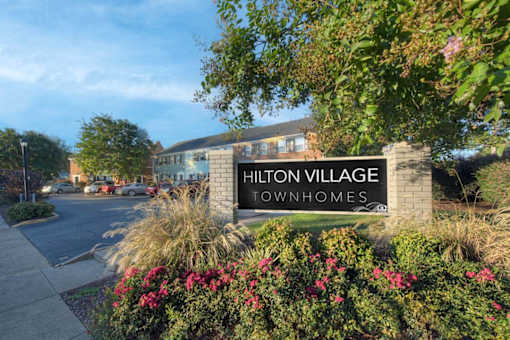 The sign for Hilton Village Townhomes is surrounded by flowers and greenery.