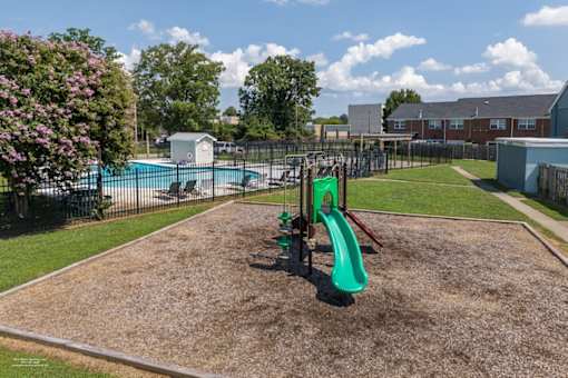A playground with a green slide and a pool in the background.