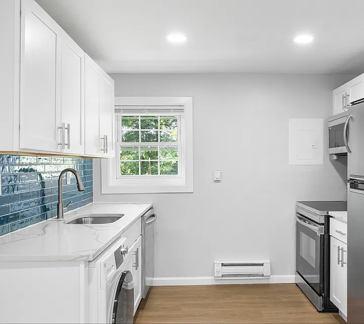 Contemporary kitchen featuring sleek stainless steel appliances, elegant blue tile backsplash, and modern white cabinetry.