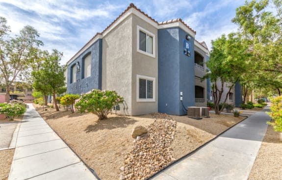 a gray and blue house with trees and a sidewalk in front of it